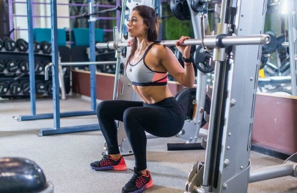 Smith squat pour les filles. Technique d'exécution sur les fesses, les genoux, une jambe, les quadriceps, frontale avec une position étroite et large